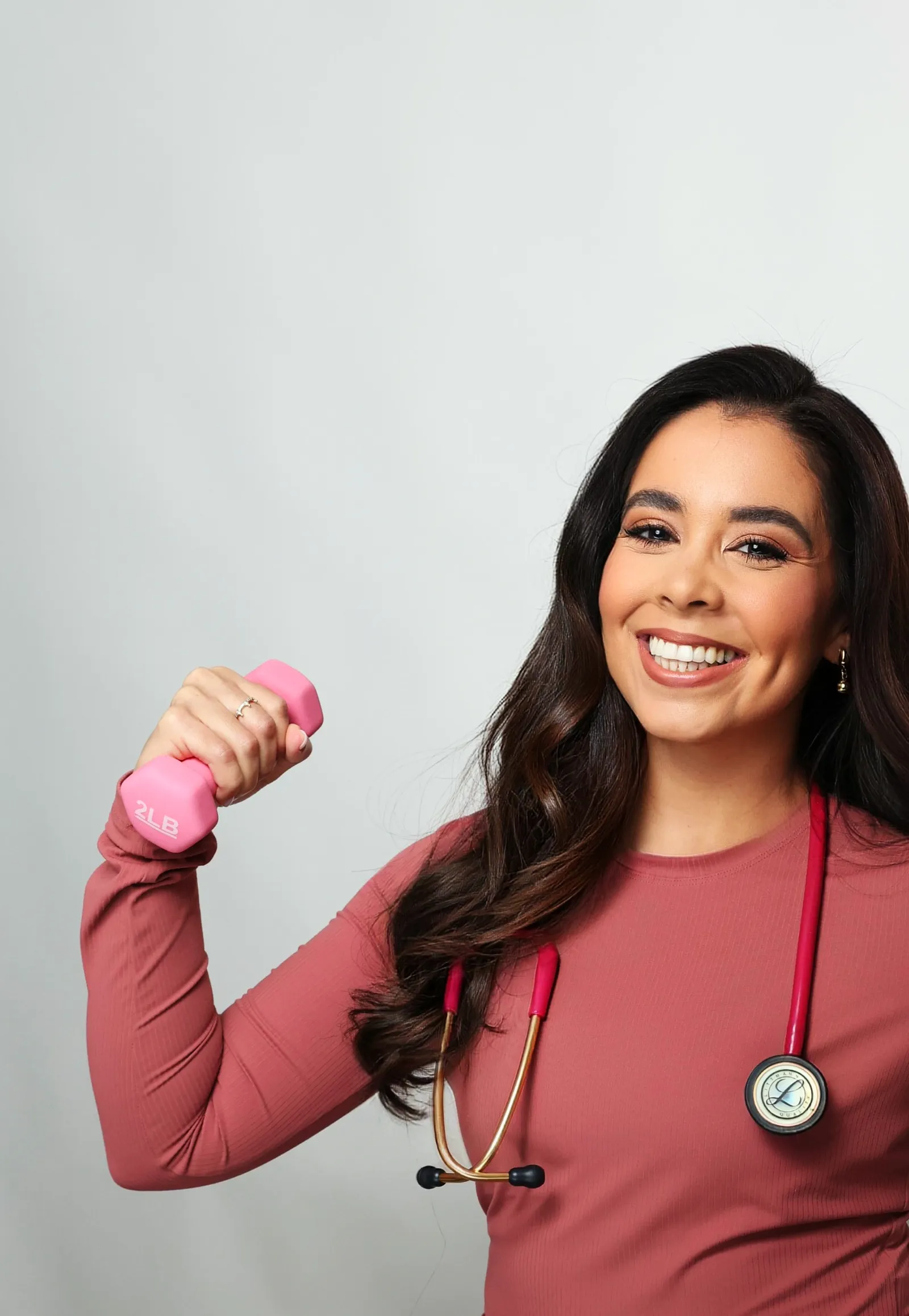 Mariene Ostolaza lifting a pink dumbbell with a stethoscope around her neck